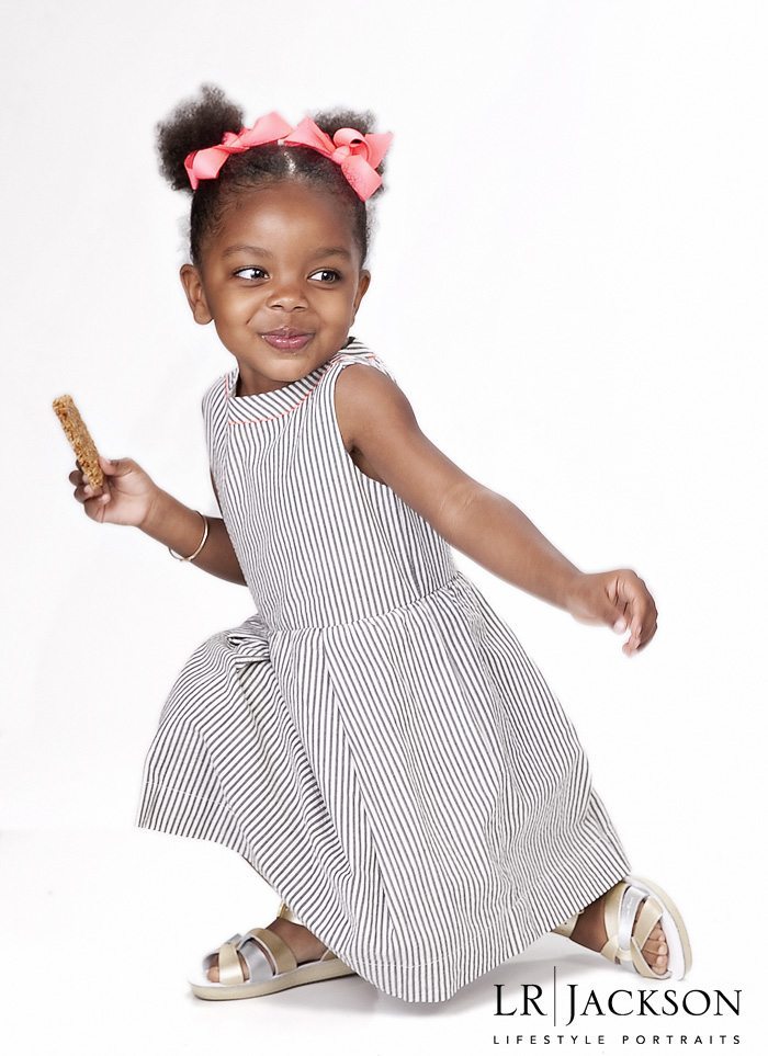 Photo of a 4yr old child in white and grey dress holding a candy bar