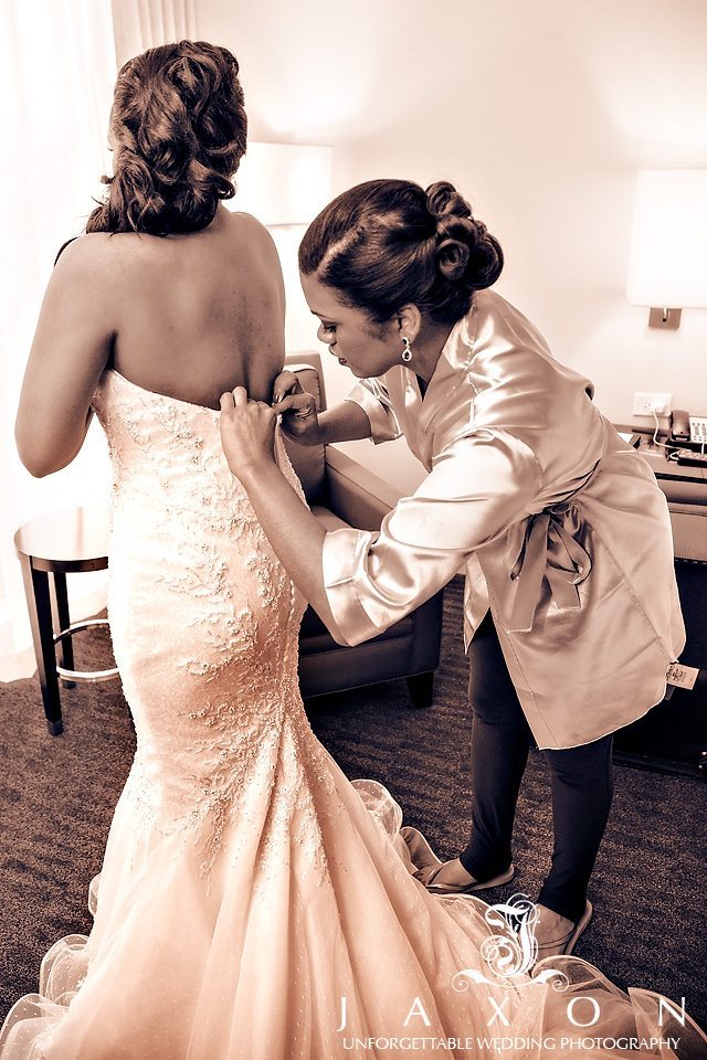 Sepia photo of bridesmaid helping bride button wedding dress in suite at Loews Hotel in Midtown Atlanta