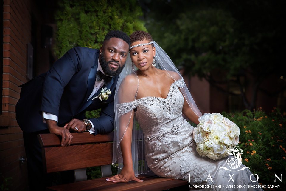 Bride sits and leans into groom as he rests on the back of park bench